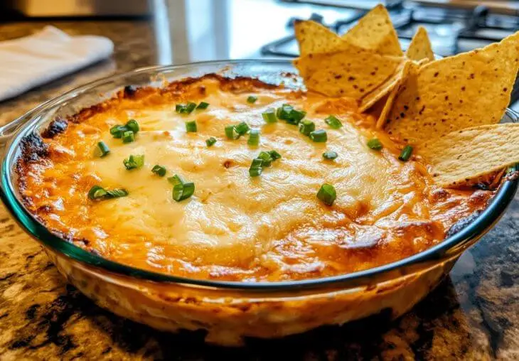 Freshly baked Buffalo Chicken Dip topped with melted cheese and green onions, served with tortilla chips