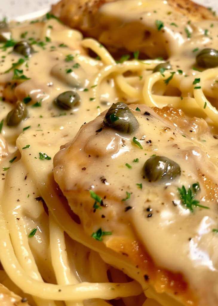 Close-up of chicken piccata pasta with creamy lemon butter sauce, capers, and parsley on spaghetti noodles.