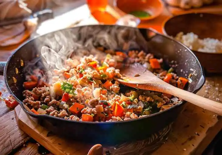 Ground turkey recipes cooking in a cast-iron skillet with carrots, onions, and herbs, steaming over medium heat in a cozy kitchen.