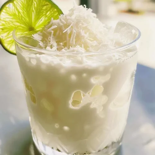 Lime and coconut cocktail topped with shredded coconut and a lime wheel served in a clear glass.