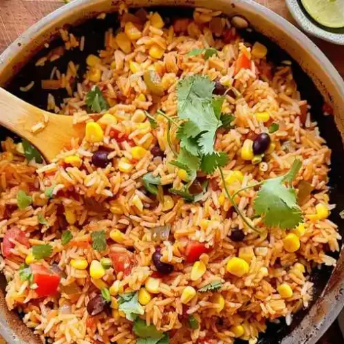 A skillet filled with Mexican side dishes rice mixed with corn, black beans, tomatoes, and cilantro, shown in a homemade kitchen style.