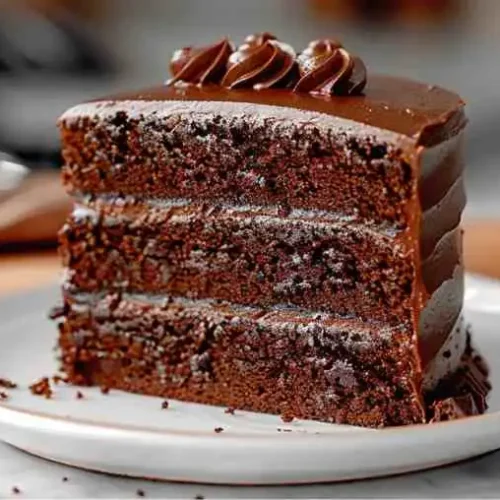 Easy Chocolate Cake Recipe (Moist & Simple) 4 A moist triple-layer Chocolate Cake Recipe slice covered in smooth chocolate frosting, served on a dessert plate.